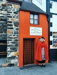 man in red robe standing in front of brown brick wall