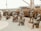 A group of life-sized bronze statues depicting military personnel in various poses. Some are standing, while others are seated or kneeling. The scene includes a figure in a wheelchair, suggesting a theme of camaraderie and inclusion. Behind the statues, there is a naval ship and some trees, adding a maritime and historical context to the scene.