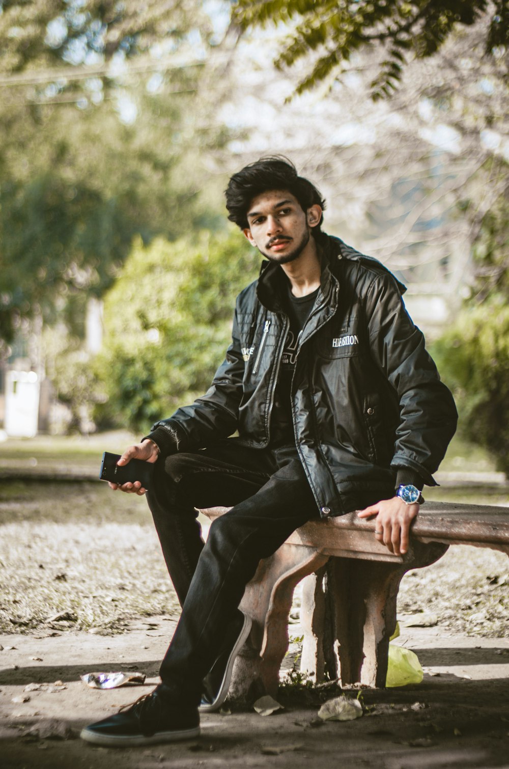 man in black leather jacket sitting on brown wooden bench during daytime