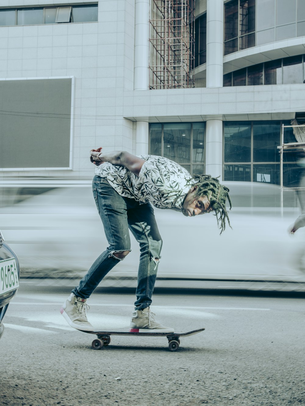 Hombre con camisa de camuflaje gris y negra y jeans de mezclilla azules montando patineta negra durante el día