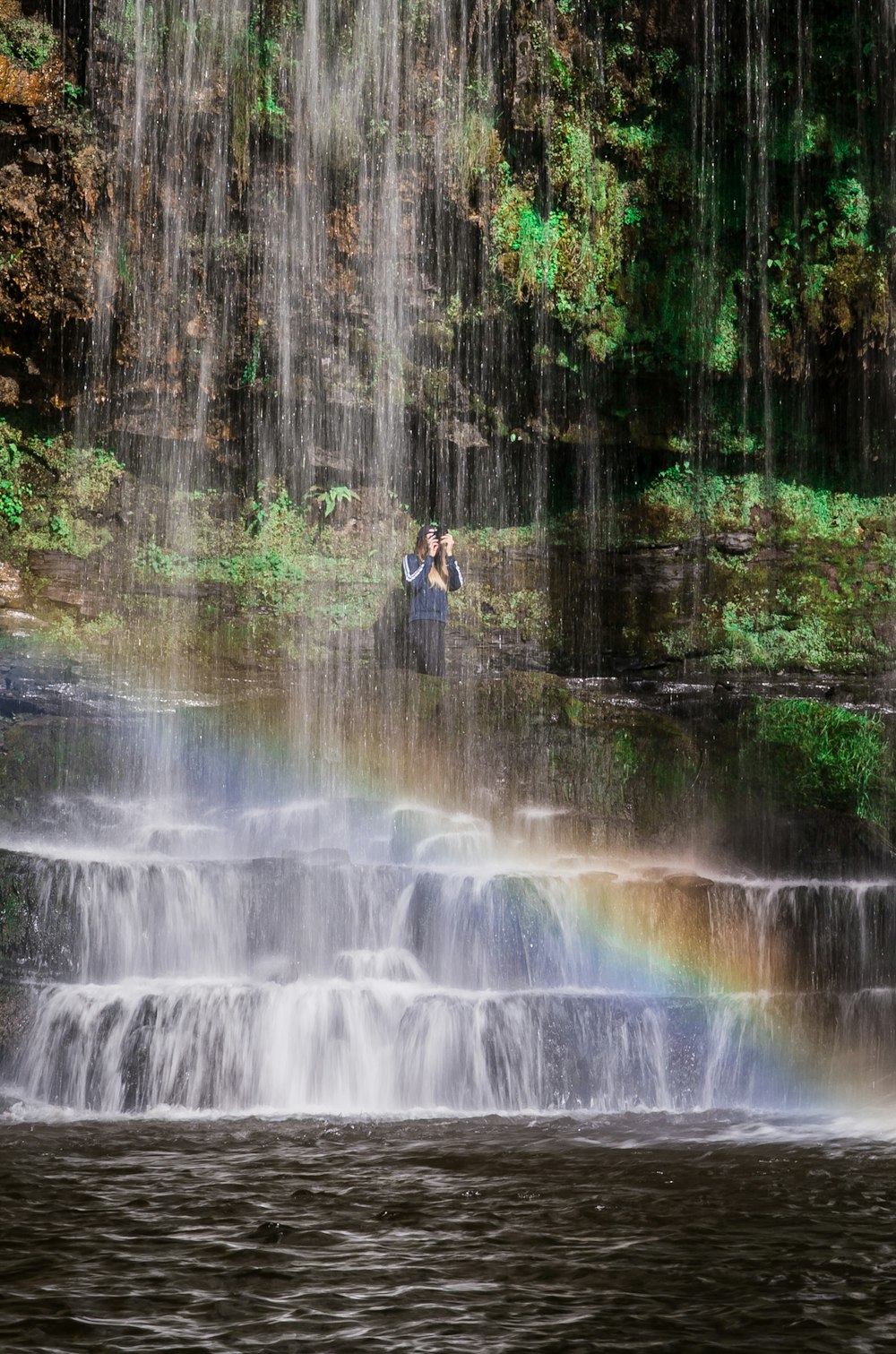 person in black jacket and black pants standing on rock near waterfalls during daytime