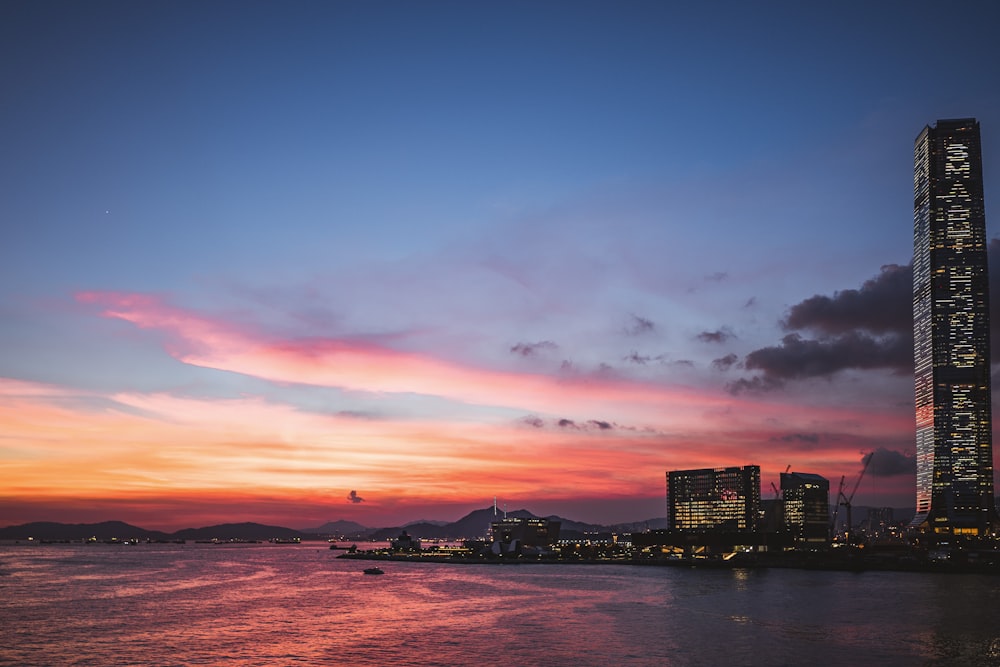 silhouette of city buildings near body of water during sunset