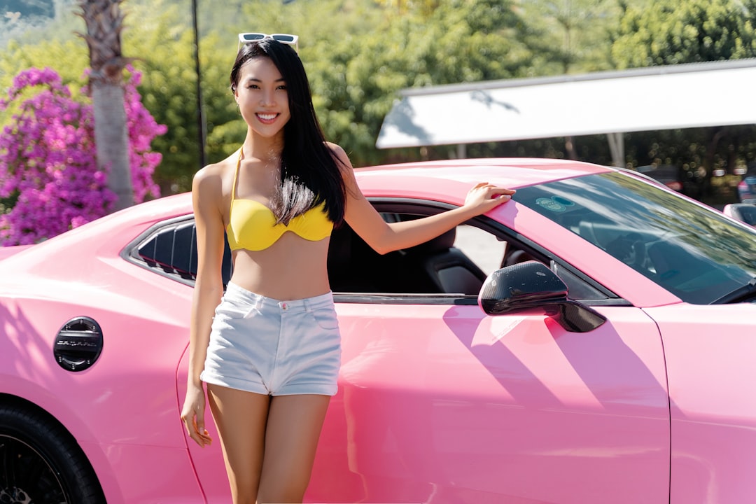 woman in black sports bra and white shorts leaning on pink car
