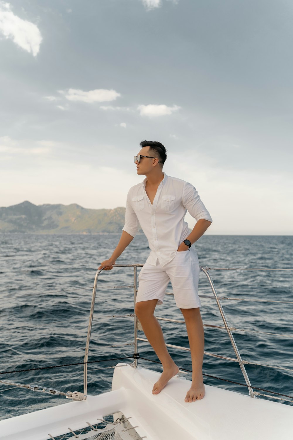 man in white polo shirt and white shorts wearing black sunglasses standing on boat during daytime