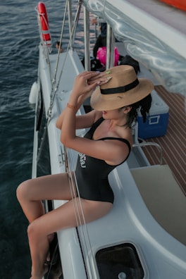 woman in black swimsuit wearing brown sun hat sitting on white boat during daytime