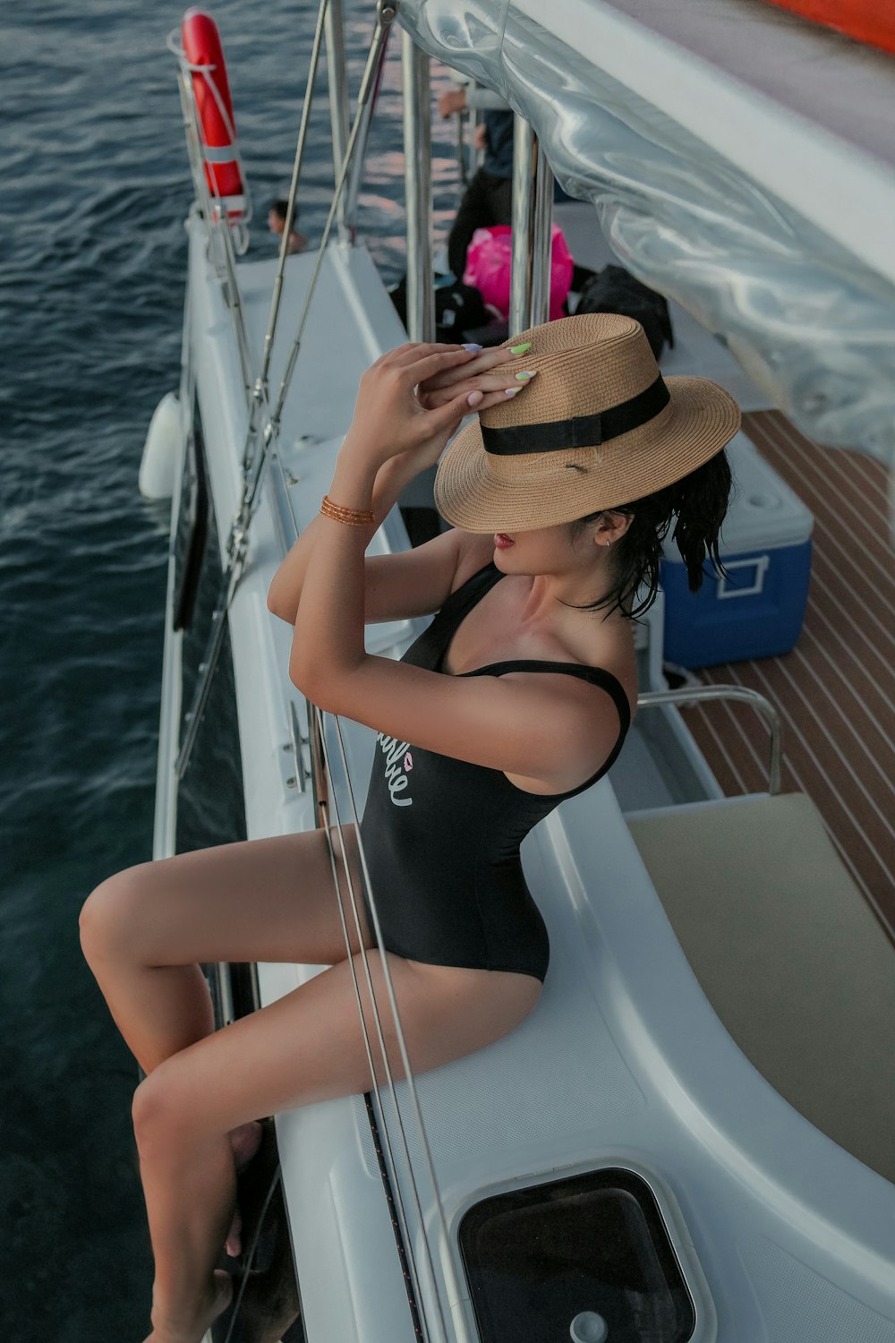 Frau im schwarzen Badeanzug mit braunem Sonnenhut sitzt tagsüber auf weißem Boot