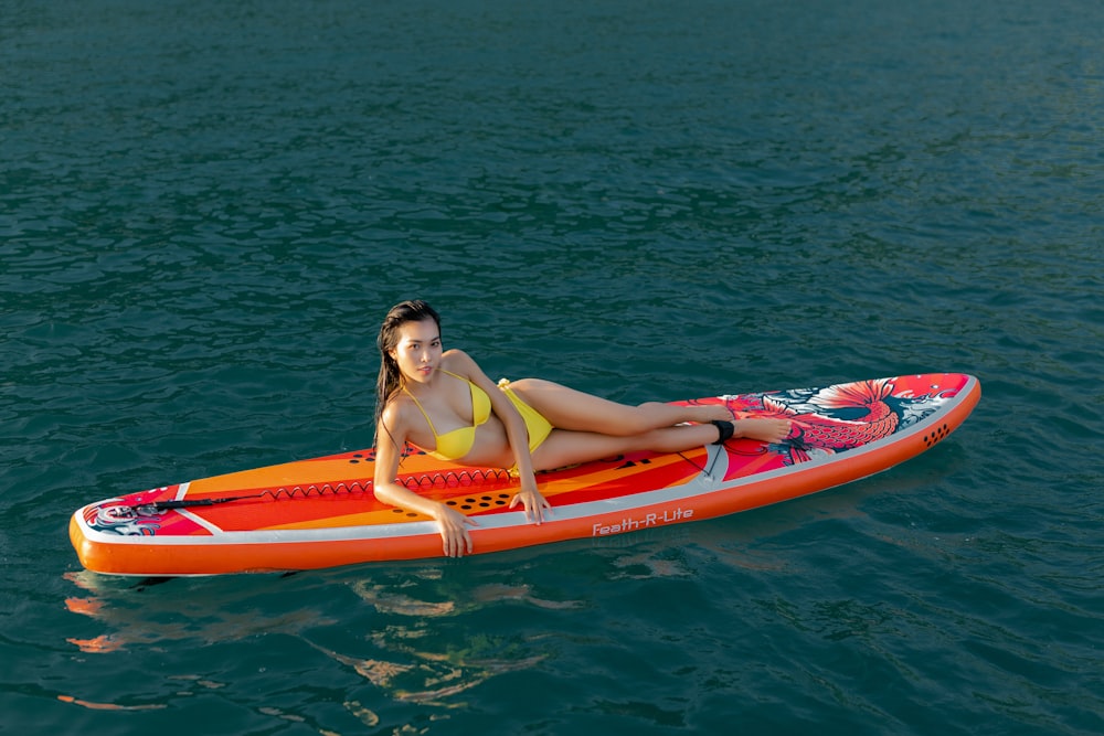 woman in pink bikini sitting on red kayak on body of water during daytime