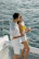 Happy couple clinking glasses on a boat with turquoise waters in the background.