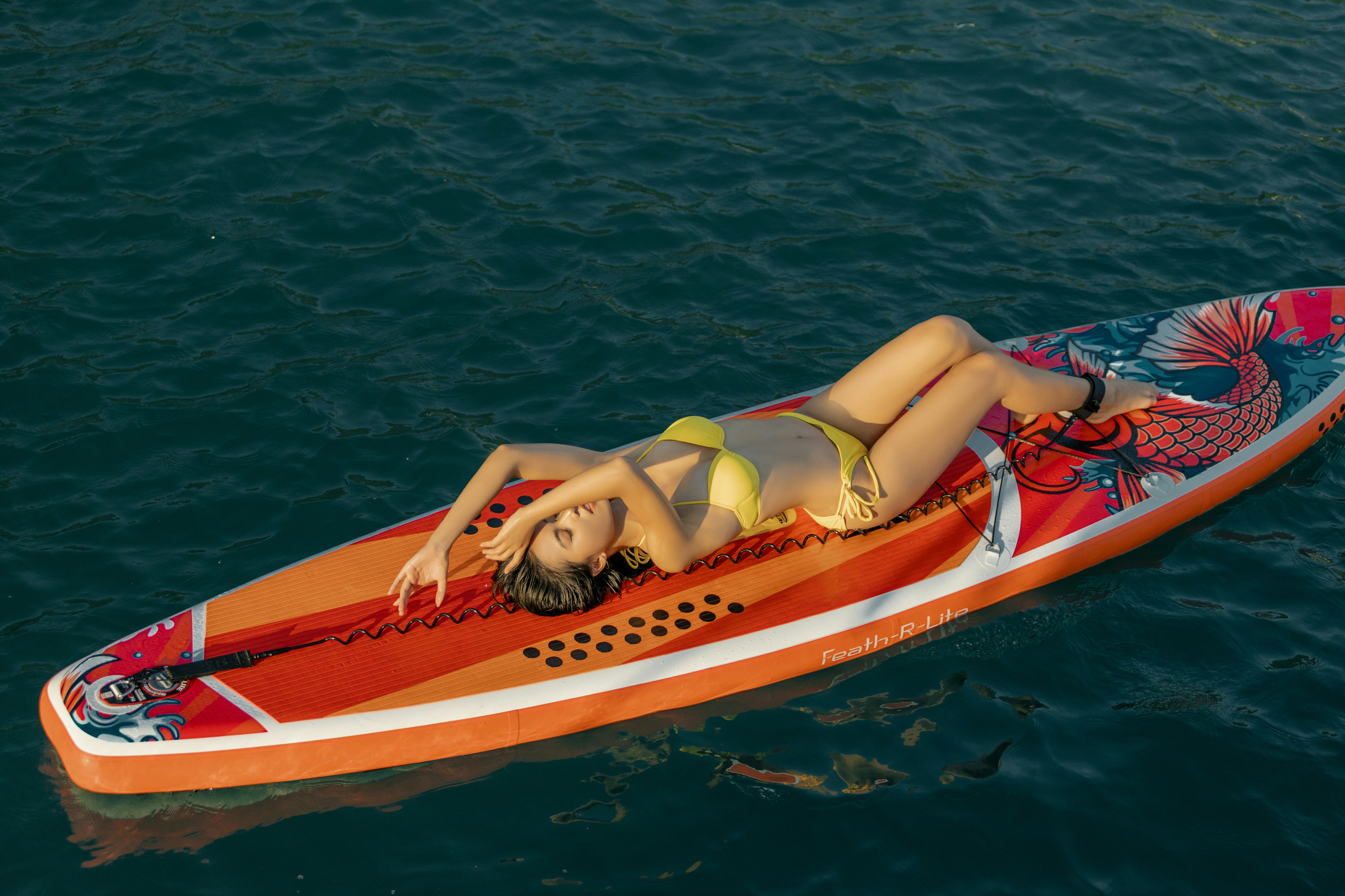 woman in red bikini lying on red and white surfboard on body of water during daytime