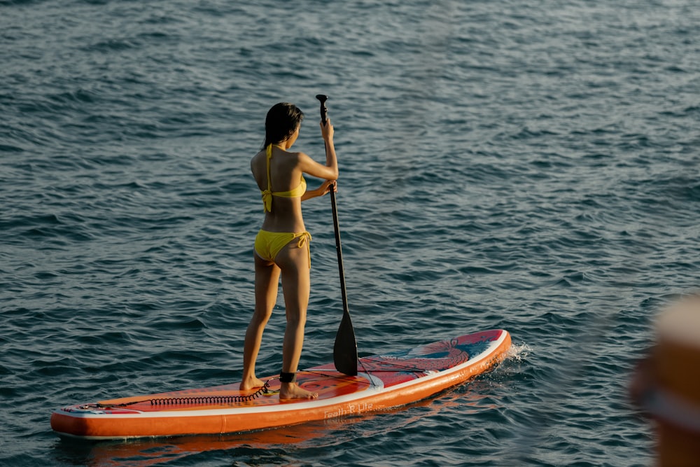 woman in yellow bikini riding on yellow and red kayak on body of water during daytime