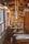 A cozy wooden workshop filled with various materials and crafted items. The space includes shelves displaying wooden crafts and tools, with sunlight streaming in through large windows on the left. Wind chimes and other decorative pieces hang from the ceiling.