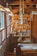 A cozy wooden workshop filled with various materials and crafted items. The space includes shelves displaying wooden crafts and tools, with sunlight streaming in through large windows on the left. Wind chimes and other decorative pieces hang from the ceiling.