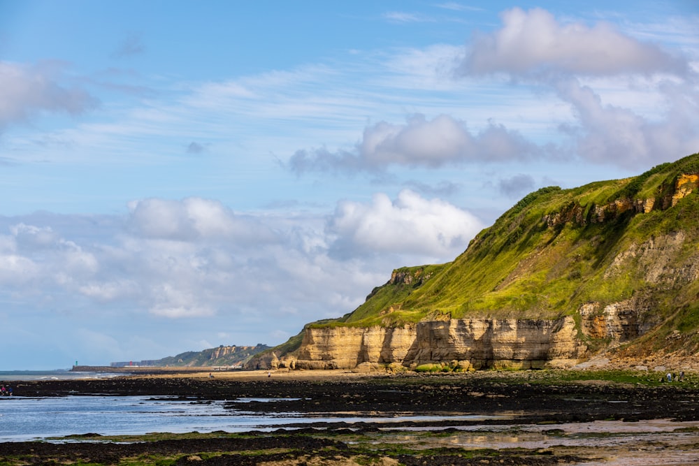 green and brown mountain beside body of water under blue sky and white clouds during daytime