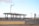 A petrol station in an empty, arid landscape, featuring multiple fuel pumps under a modern canopy. The station's branding is visible with signs in both English and Arabic. The environment appears deserted, with a clear blue sky and distant hills, creating a sense of isolation.