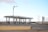 A petrol station in an empty, arid landscape, featuring multiple fuel pumps under a modern canopy. The station's branding is visible with signs in both English and Arabic. The environment appears deserted, with a clear blue sky and distant hills, creating a sense of isolation.