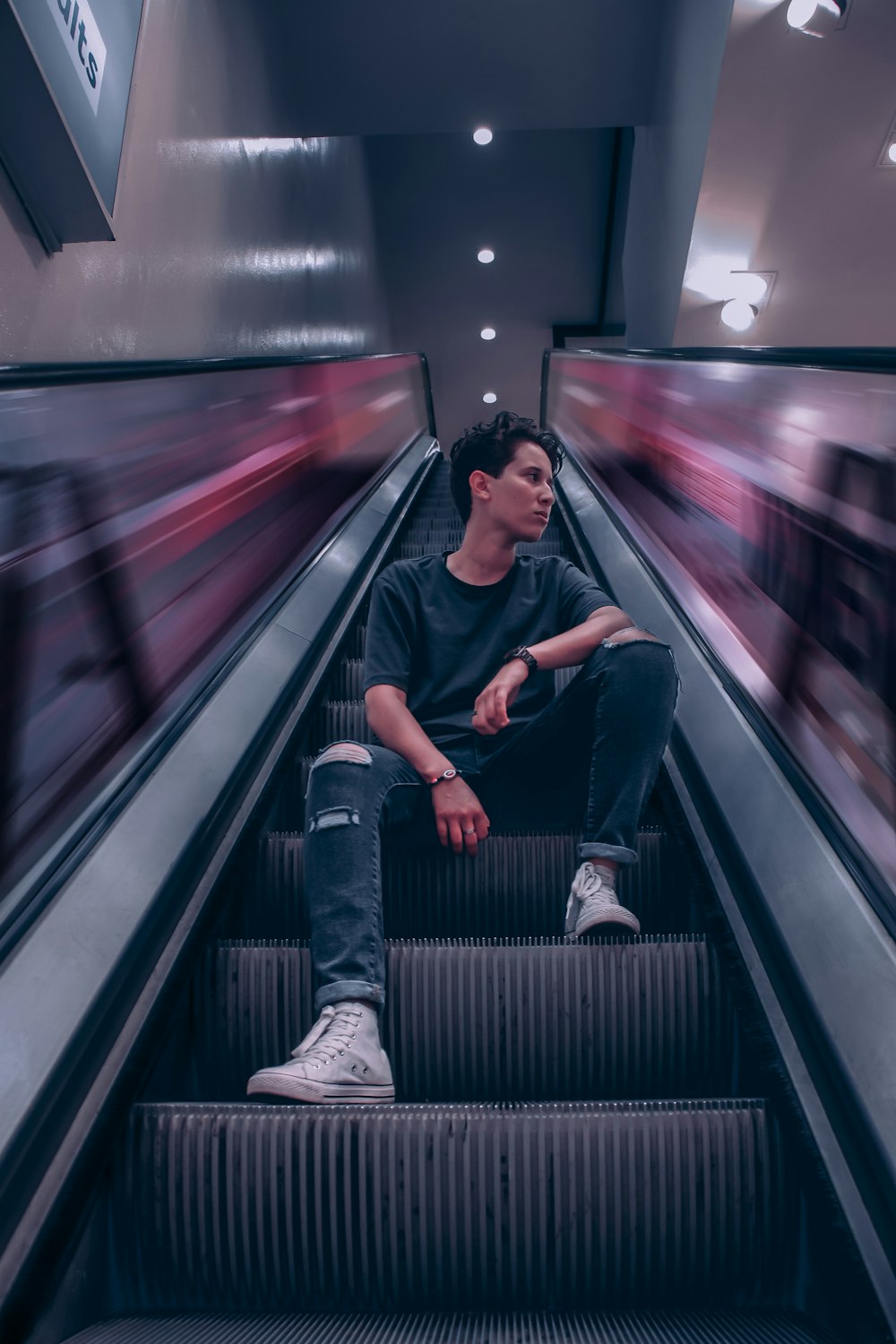 man in black t-shirt and blue denim jeans sitting on escalator