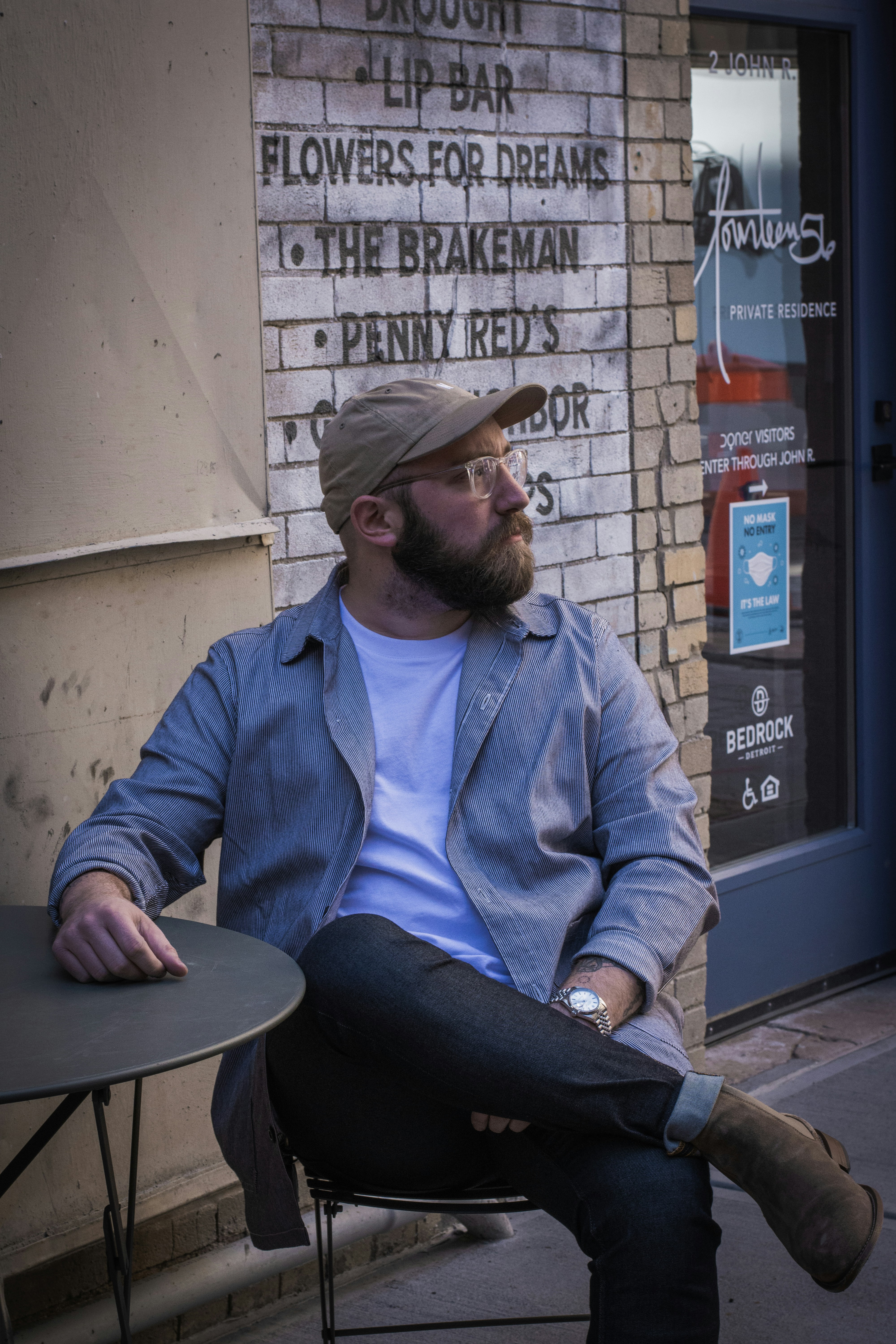 Homme en veste zippée bleue et chapeau marron assis sur une chaise