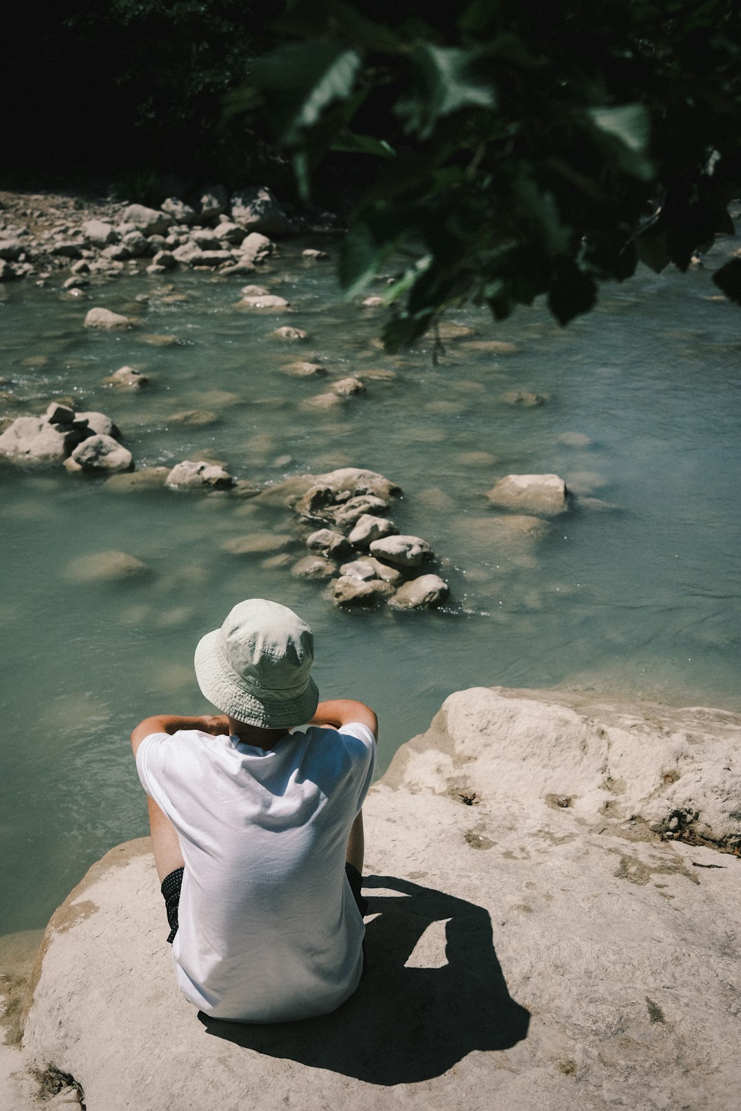 man in white shirt sitting on rock near river during daytime