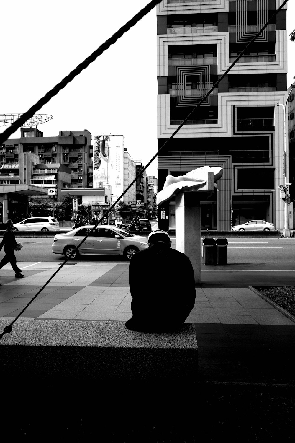 grayscale photo of man in black jacket and pants walking on sidewalk