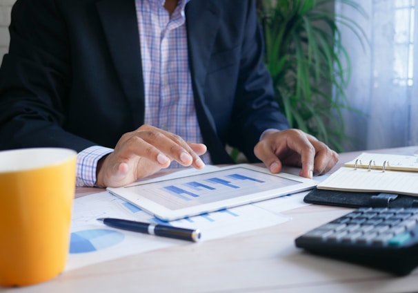 person in black suit jacket holding white tablet with financial graphs on it