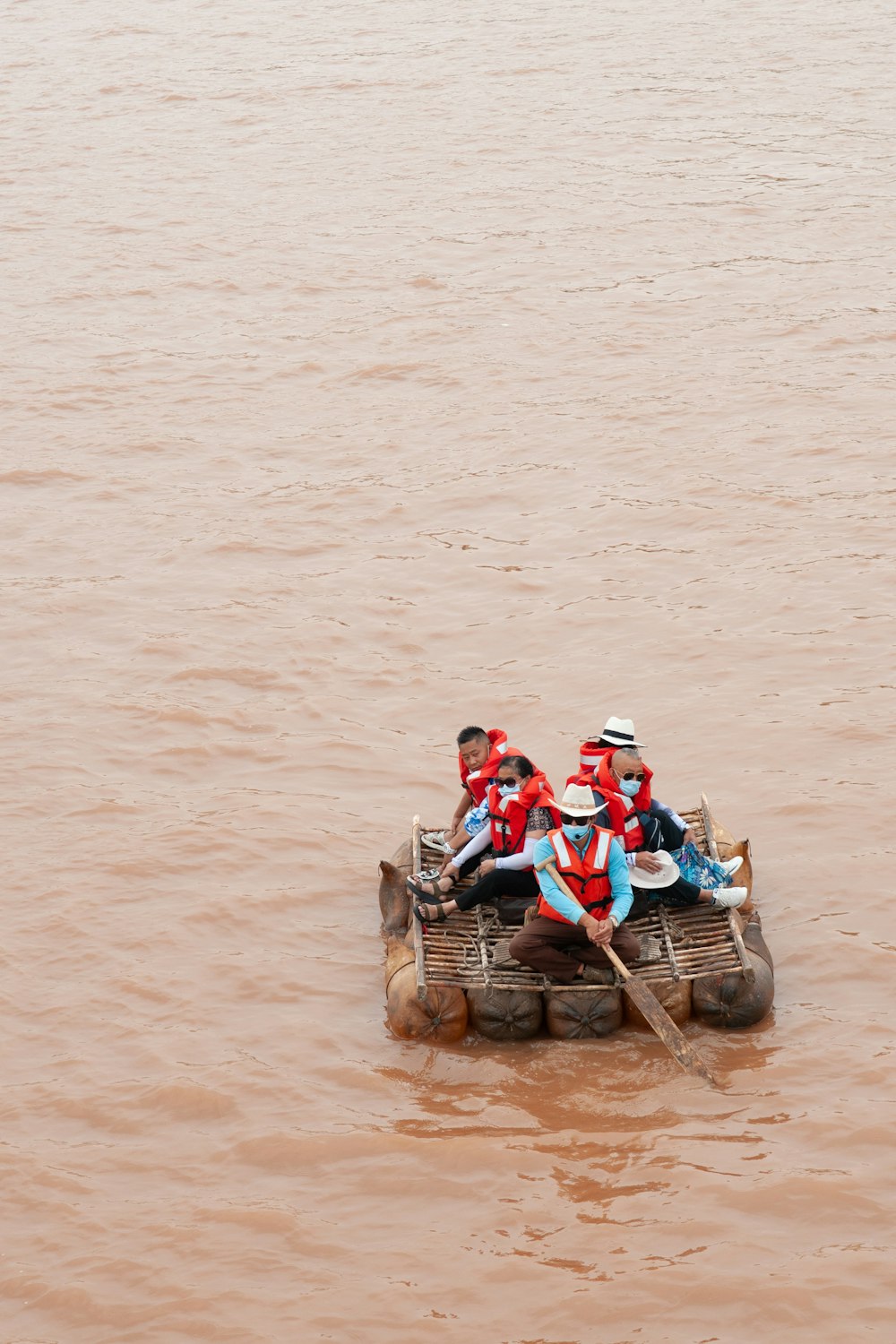 昼間、水上を茶色のボートに乗っている赤と白のシャツを着た2人の男性