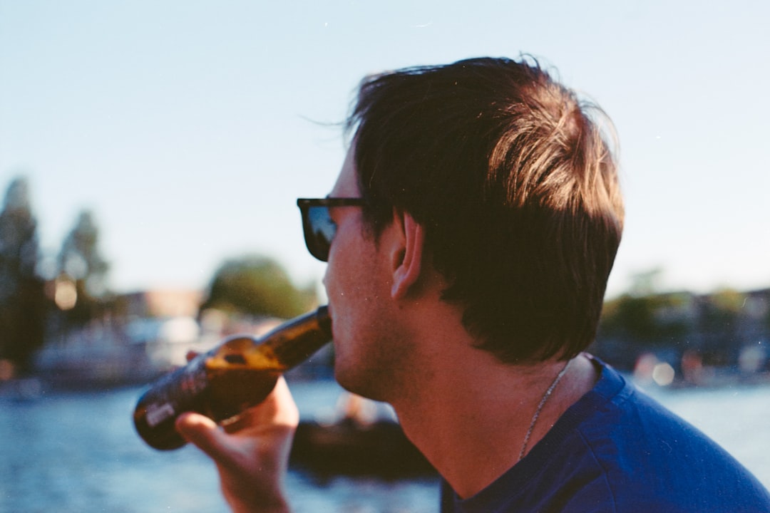man in blue crew neck shirt wearing black sunglasses drinking from bottle