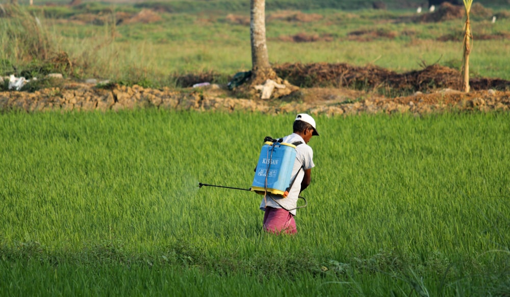 man in white t-shirt and blue denim shorts with blue backpack walking on green grass