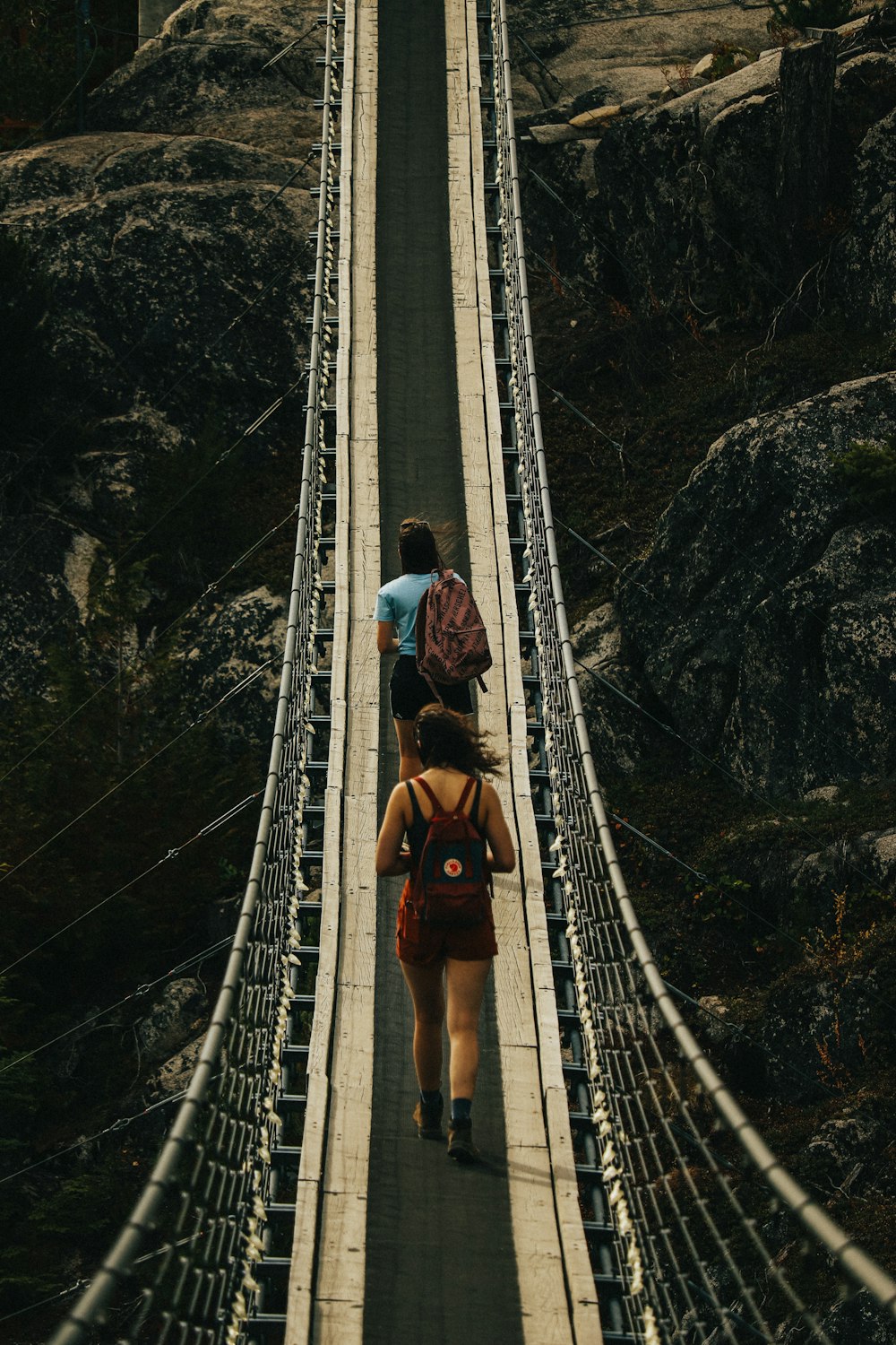 man in brown jacket and black pants walking on hanging bridge