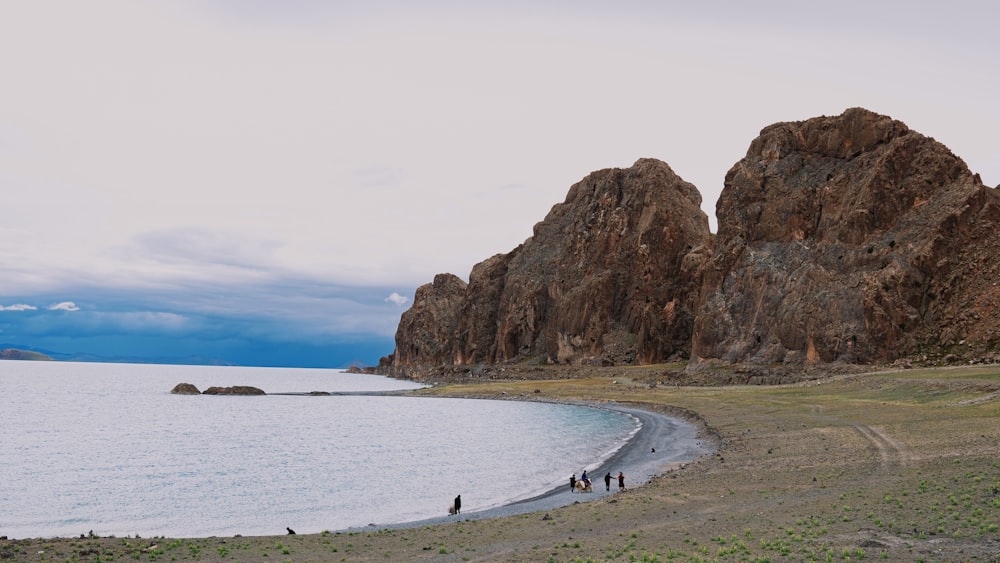 people walking on beach shore near brown rock formation during daytime