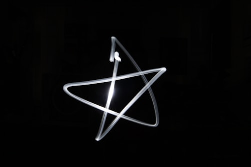A light painting of a star shape against a dark background. The image captures the smooth, bright white lines in motion, creating a glowing effect.