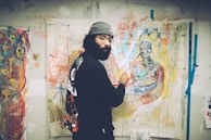 An artist is painting in a brightly colored studio filled with abstract artworks. The wall is covered with expressive and vibrant paintings. The artist, dressed in casual, artistic attire, focuses on a canvas depicting a figure.