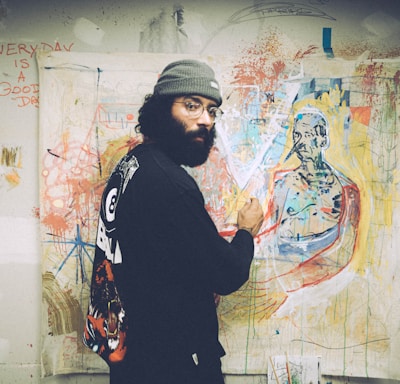 man in black and white sweater standing beside wall with graffiti