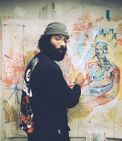 man in black and white sweater standing beside wall with graffiti