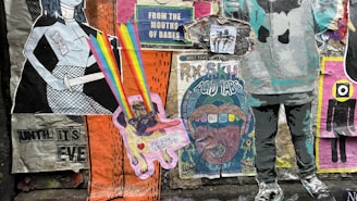 A collage of colorful street art posters on a wall, featuring a variety of graphic designs and styles. One poster has a cartoonish character emitting rainbow beams from its eyes, while another displays text about 'acid tabs'. There are printed images of people, abstract patterns, and cutouts of human figures.