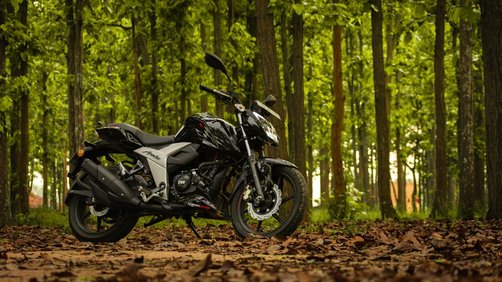 black and silver motorcycle parked on brown dirt road in forest during daytime