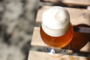 A close-up photo of a frosty pint of craft beer with a rich amber color and a creamy head, set against a rustic wooden table in the old town center brewery.