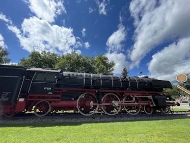 A vintage steam locomotive on display at a railroad museum surrounded by lush greenery.