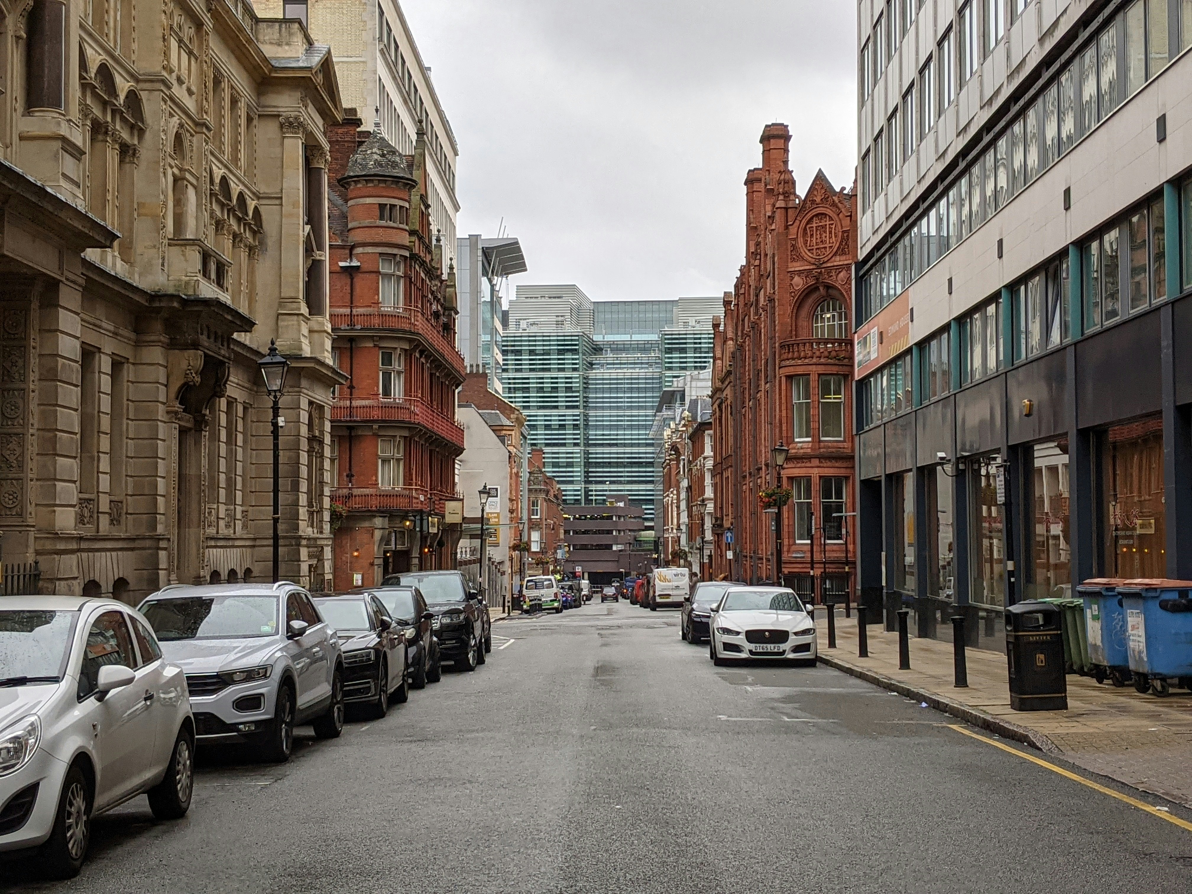 cars parked on side of the road in between high rise buildings during daytime