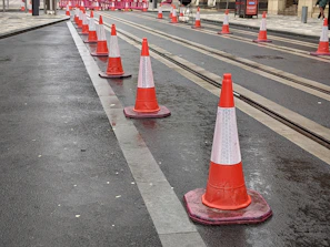 A team of safety professionals setting up bright orange traffic cones and signage on a busy Malaysian road.