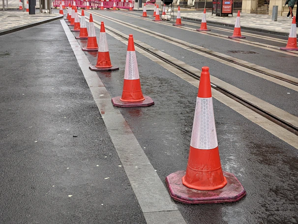 A row of bright orange traffic cones lined up along a busy Mumbai street.