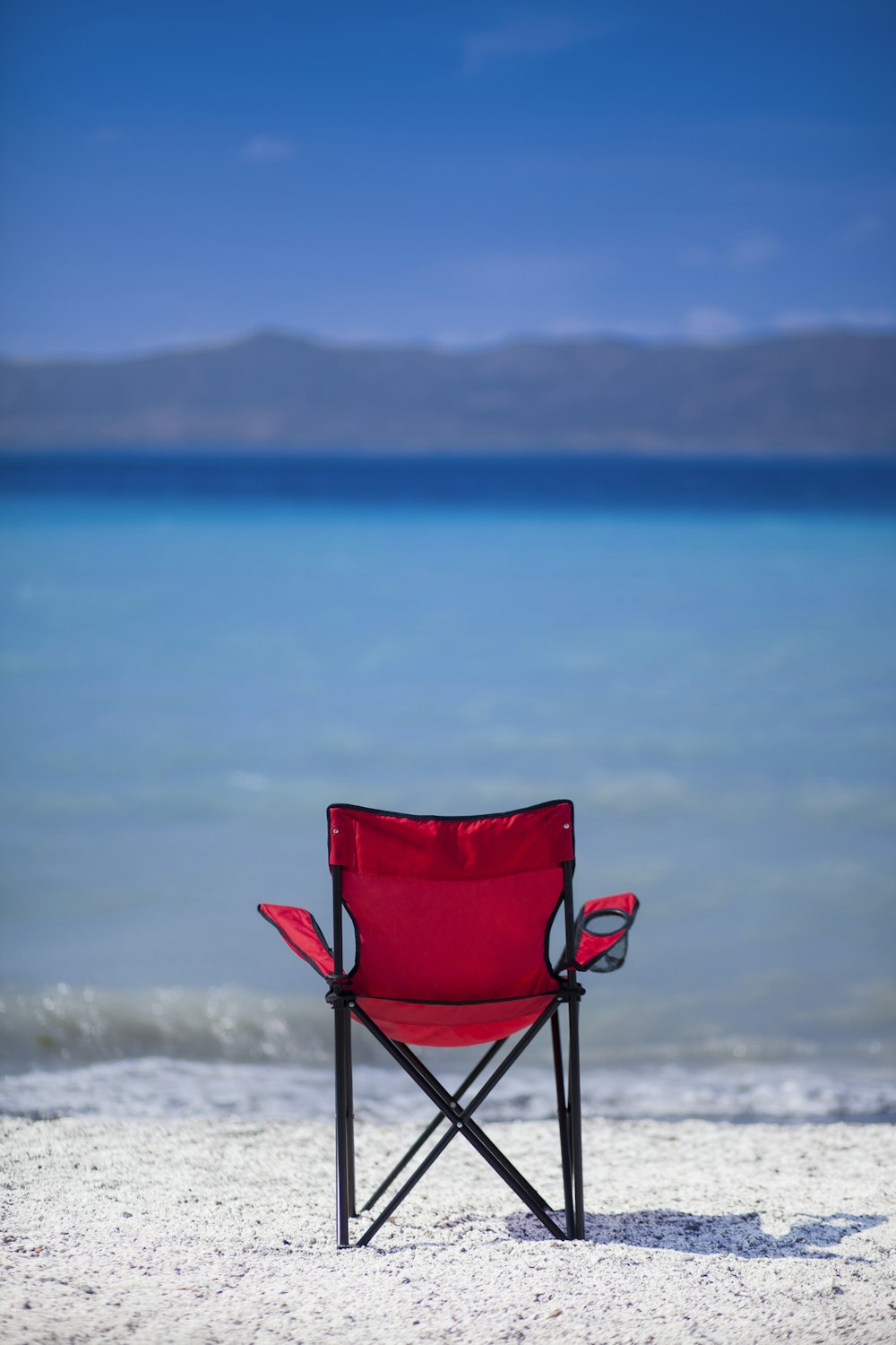 a red chair sitting on top of a sandy beach