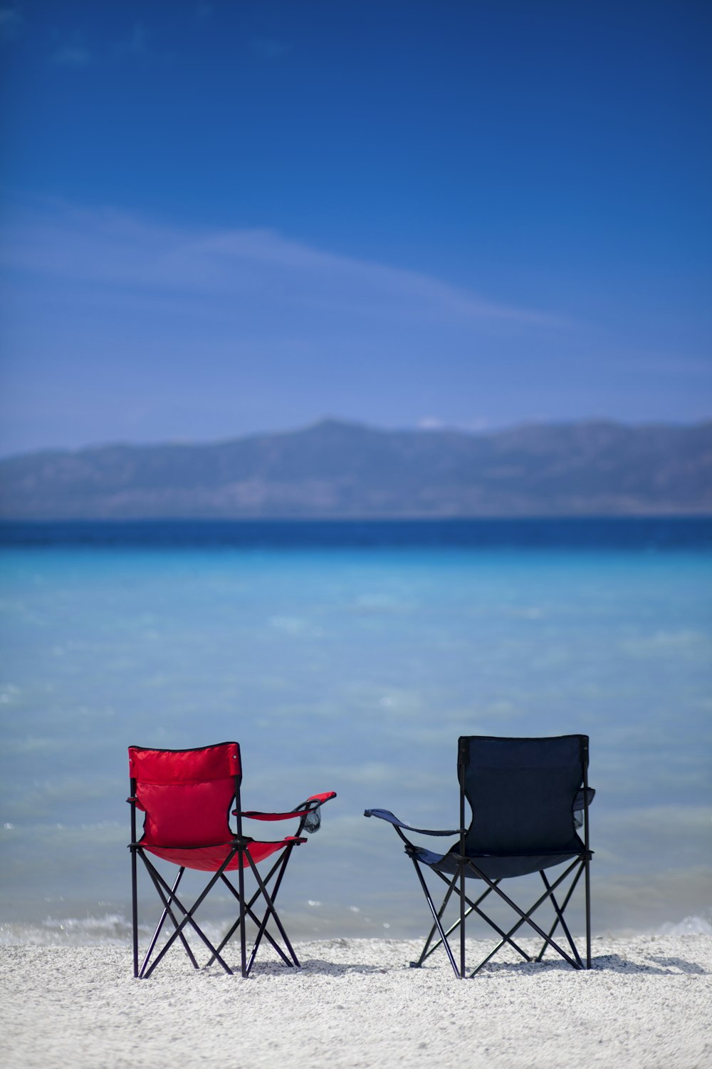 red and black camping chair on gray sand near body of water during daytime