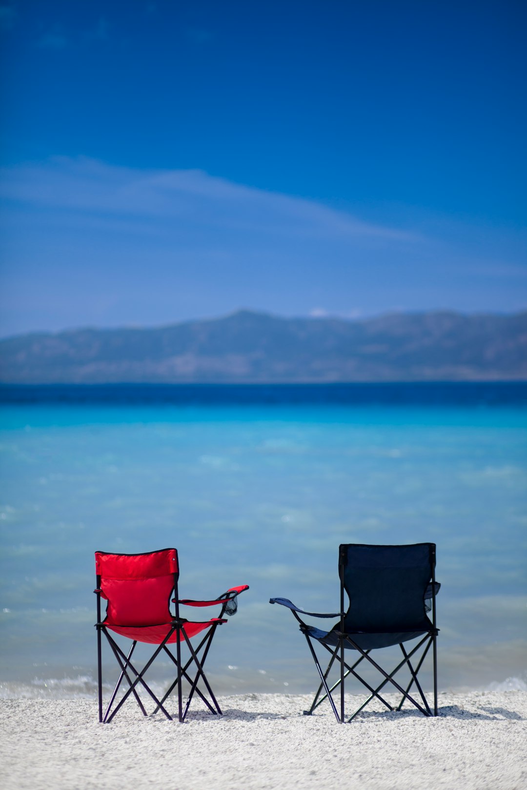 red and black camping chair on gray sand near body of water during daytime