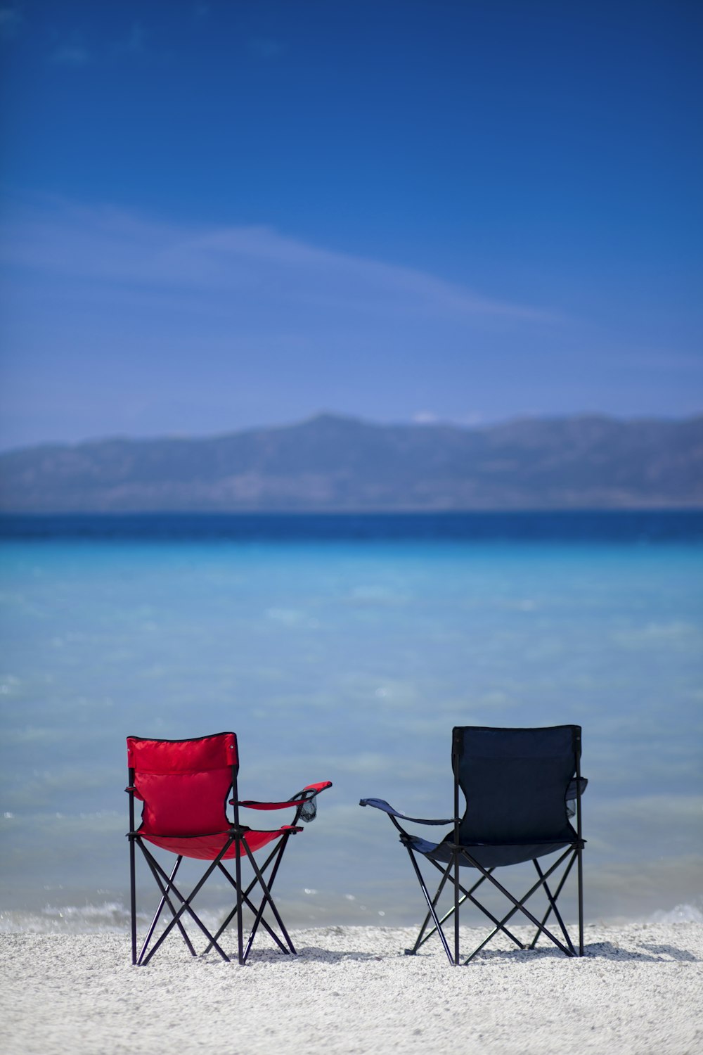 Chaise de camping rouge et noire sur le sable gris près du plan d’eau pendant la journée