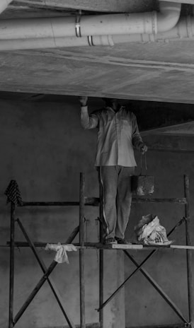 grayscale photo of man standing on ladder