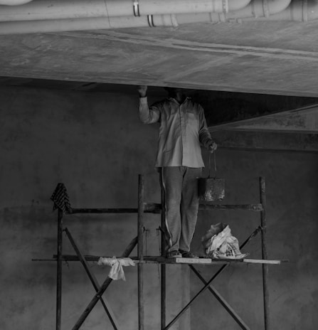 grayscale photo of man standing on ladder