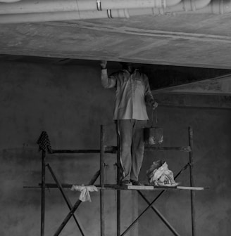 grayscale photo of man standing on ladder