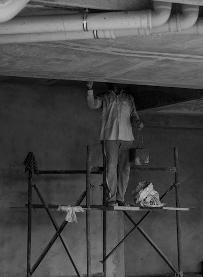 grayscale photo of man standing on ladder