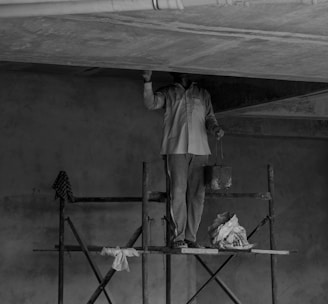 grayscale photo of man standing on ladder