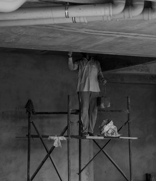 grayscale photo of man standing on ladder